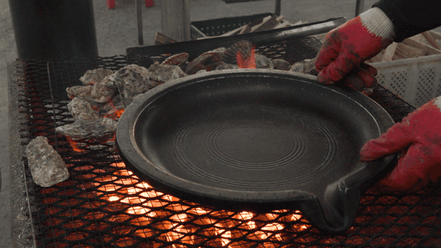 Grill plate placed next to grilled oysters over fire