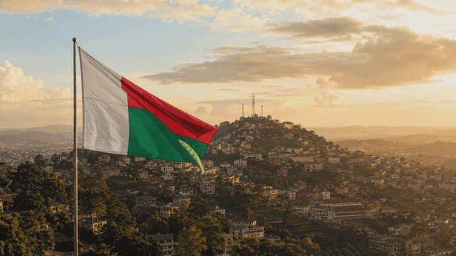 Madagascar flag fluttering over village landscape at sunset