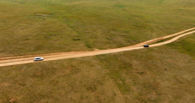 Two cars driving on a dirt road in a vast field