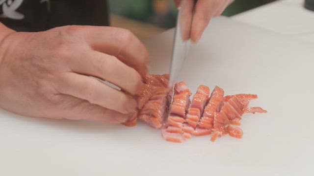 Smoked duck being cut with a knife on a cutting board in the kitchen