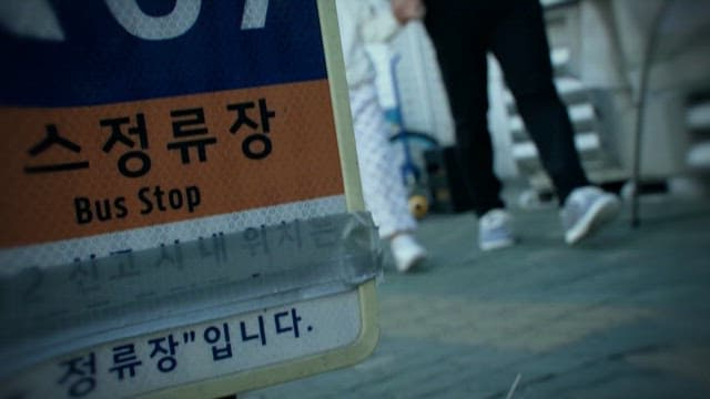 Child and Adult Passing by a Bus Stop Sign