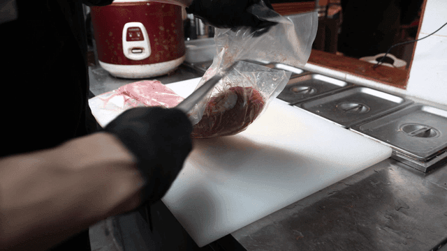 Chef cutting plastic bag containing raw meat with knife in kitchen