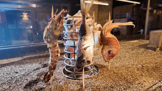 Raw grilled fish skewered next to charcoal in cylinder