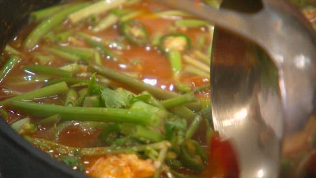 Stirring the stew with fresh vegetables using a ladle and spoon