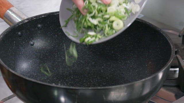 Chopped Green Onions Being Added to a Black Frying Pan