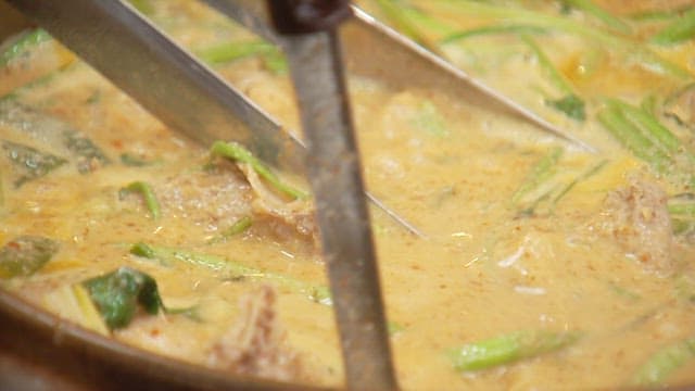 Ladleful of rich and savory duck soup being served in a bowl