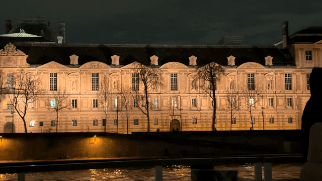 Historic European buildings illuminated at night, seen from boat on river