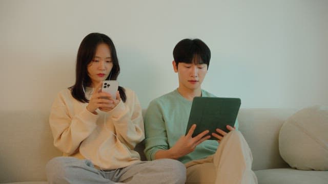 Two people using digital devices on a sofa in cozy living room