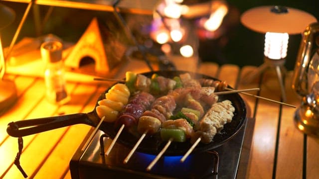 Skewered meat cooking on a pan over a gas burner at night