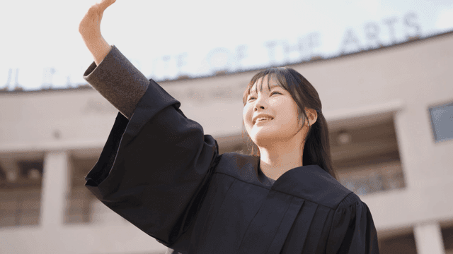 Graduates wearing academic gowns and smiling while greeting