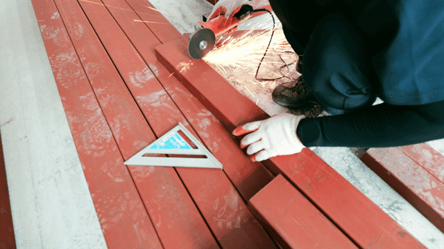 Worker cutting red metal beam with grinder