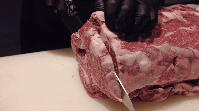 Large piece of beef is being cut on a cutting board.