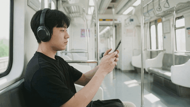 Man wearing wireless headset and looking at his phone on subway