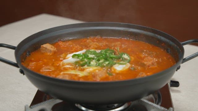 고추 고명이 올라간 채 끓고 있는 매운 김치찌개 냄비
