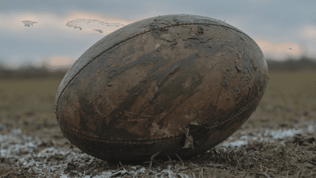 Old rugby ball on muddy field.