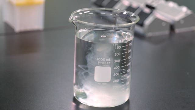 실험실 책상 위 물이 든 비커에 스포이드로 노란 액체를 넣는 모습