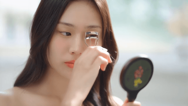 Woman using eyelash curler while looking in the mirror in a bright room