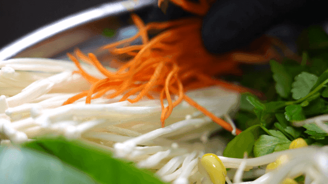 Hot pot topped with carrots and enoki mushrooms