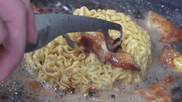 Flipping ramen over a sizzling pan with tongs