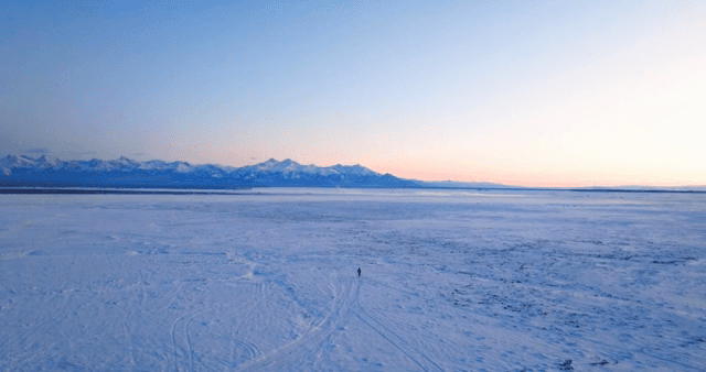 Lone figure walking across a vast snowy landscape