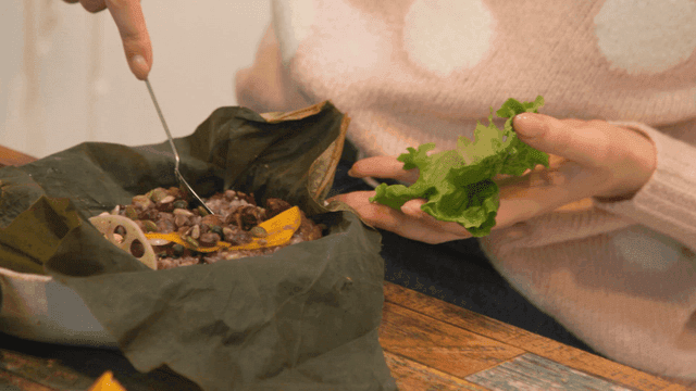 Person holding spoon for scooping lotus leaf rice and lettuce.