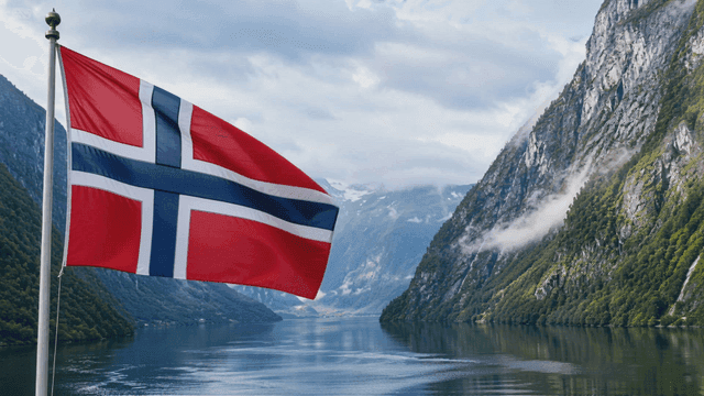Norwegian flag waving by a fjord