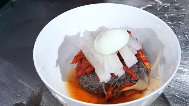 명태회냉면에 얇게 썬 오이를 넣는 장면