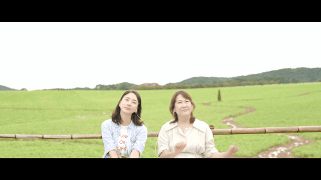 Two women peacefully listening to music together with earphones in field