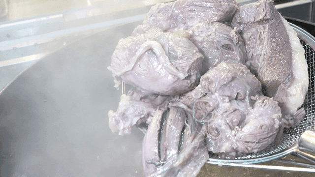 Boiled beef scooped out of large pot with sieve