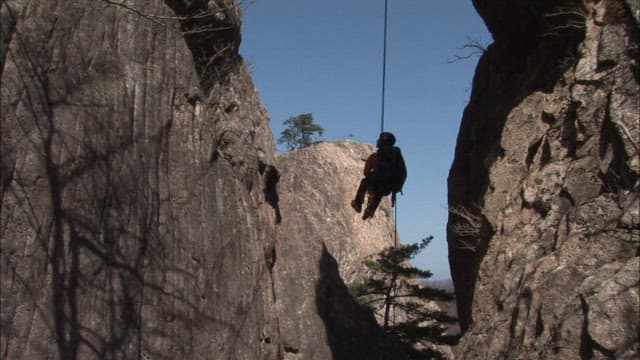 Rock Climber Rappelling Down a Mountain Cliff