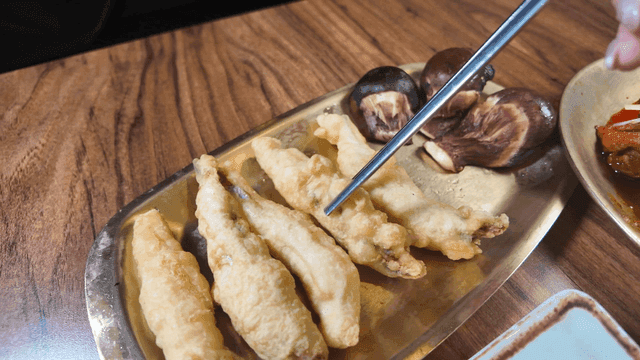 Chopsticks picking up fried anchovies on plate and mushrooms