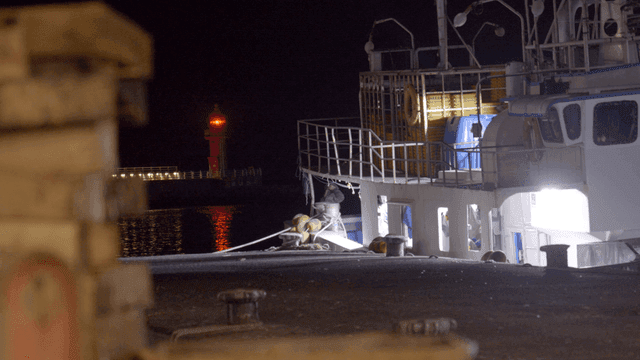 A docked ship at night with a lighthouse