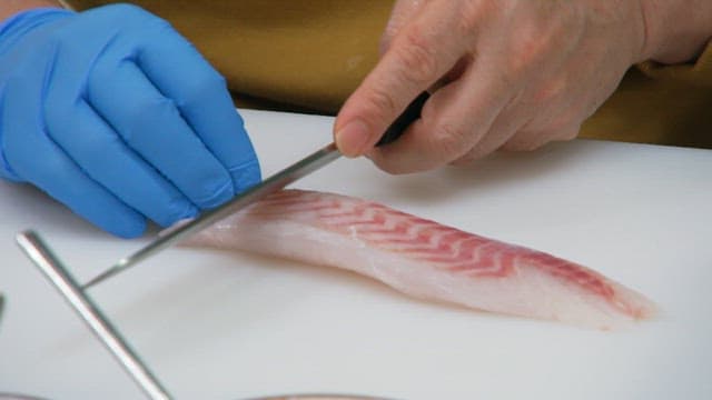 Slicing raw fish delicately with a knife on a cutting board