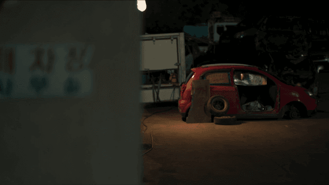 어두운 폐차장 사무실에서 나오는 여성과 빨간 차