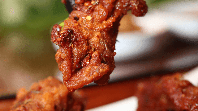 Glove-wearing hand picking up spicy Xiangla lamb ribs loaded with sauce