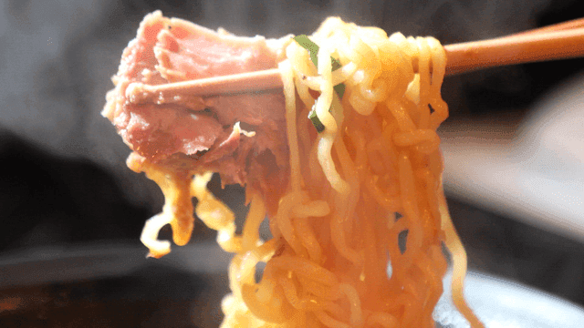 Chopsticks holding ramen with meat