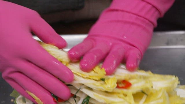 Preparing fresh cabbage kimchi with rubber-gloved hands