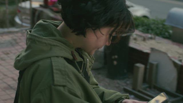 길거리에서 핸드폰을 들고 전화 통화를 하는 녹색 재킷을 입은 사람