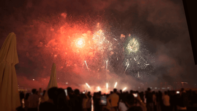 Fireworks above city skyline, watched by large crowds