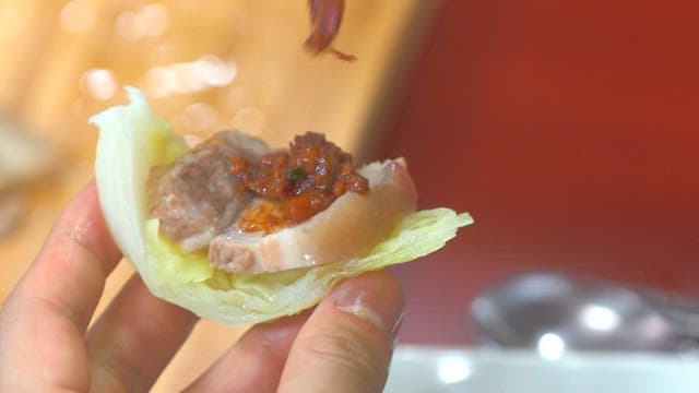 Making a Korean wrap with boiled pork, cabbage, and kimchi