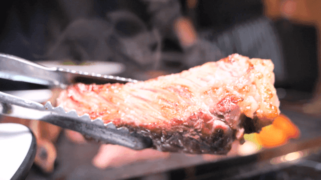 Grilled beef picked up with tongs from grill