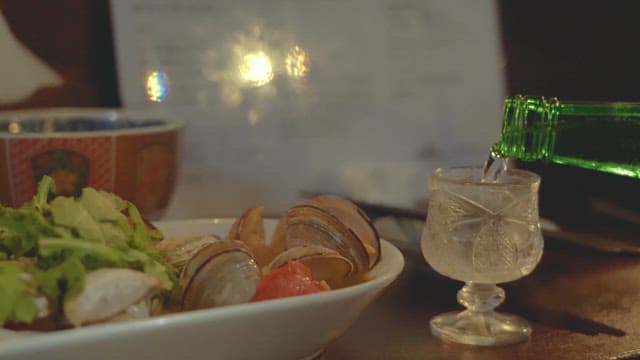 테이블 위 조개찜 옆 술잔에 따라지는 소주