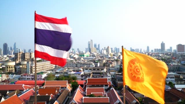 Thai national flag and Dharma Chakra flag fluttering above cityscape