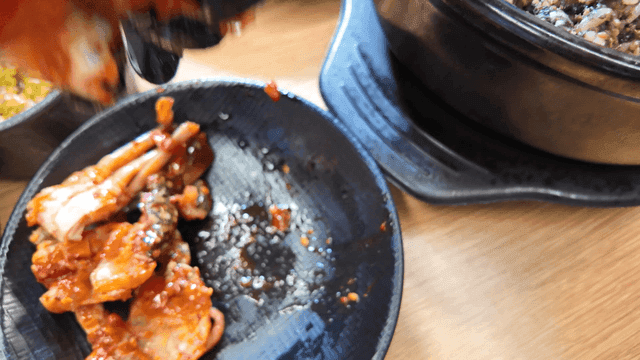 Glovenly hand placing seasoned crab on stone pot rice