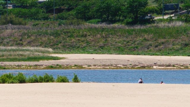 People sitting by the riverside on a sunny day surrounded by lush greenery