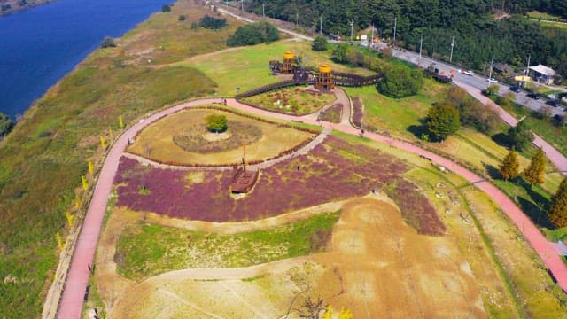 View of a lush riverside park with winding paths and a wooden structure on a sunny day