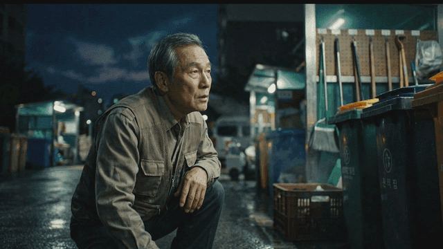 Elderly security guard crouching in apartment recycling area on dark night