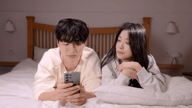 Couple talking in bed while looking at smartphone