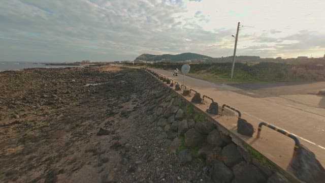 Two people riding a scooter along a coastal road