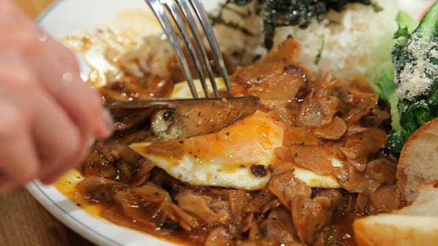 Cutting a hamburger steak with a fried egg and sauce